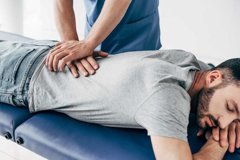 A therapist guides a patient through a stretching exercise beside a treatment table.